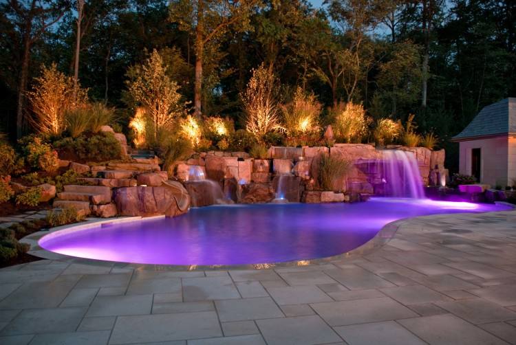 This natural swimming pool design features a raised spa, sun shelf and  water slide